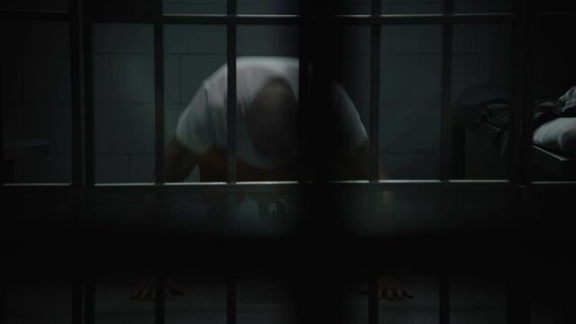 Male prisoner in orange uniform warms up, exercises and does push ups in prison cell. Tattooed criminal or inmate serves imprisonment term for crime in jail. Detention center or correctional facility.