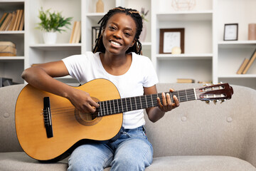 Woman in casual clothes playing acoustic guitar on sofa. Concept of music hobby, relaxation, and...