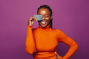 Happy woman paying with a card against a vibrant purple background - 751162670