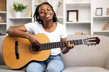 Happy Woman at home expressing joy while playing guitar, exemplifying leisure activities and...