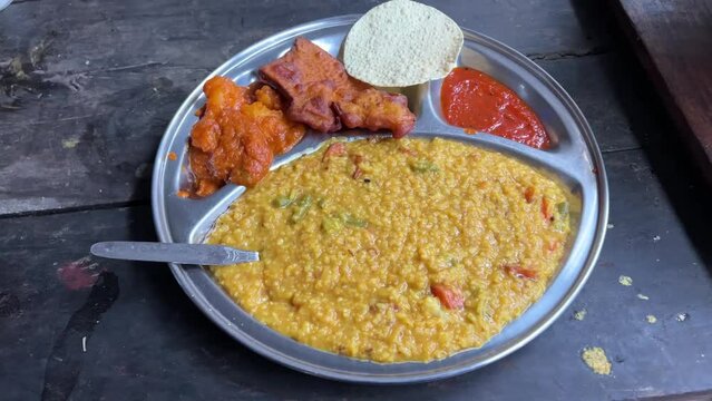 Khichuri with alu dum, chutney and papad served on a plate by a Bengali restaurant.
