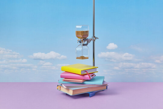 Hourglass on metal holder above stack of books.