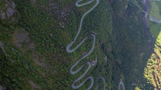Aerial top down view of tight twisting serpentine road as it winds up the steep, tree covered valley side of a Fjord in Norway.