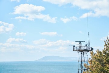 A radar tower for transmitting a signal. The top point. The sea and mountains are in the background.
