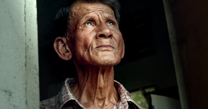 An Asian man who is an elderly worker, opened the door and looked up at the sky as if something had happened to the earth's atmosphere. Used in film concepts, humanity, documentaries and others.