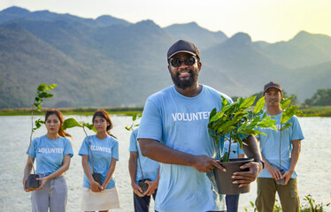 portrait african male in blue volunteer T-shirt holding pot of young sprout plant tree,concept of volunteering,reforestation,conservation of natural resources and the environment - Powered by Adobe