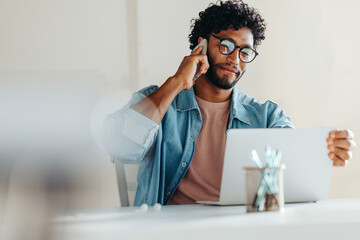 Focused young man working on laptop while on a phone call