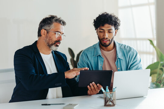 Two professional men collaborating in modern office using tablet and laptop - Powered by Adobe