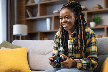 Afro American woman smiling, deeply engaged in playing video games on the console, creating a...