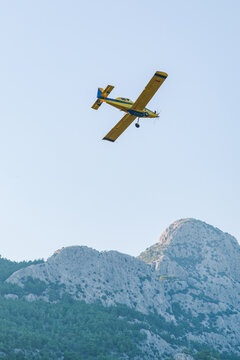 A small yellow firefighting plane flies over the mountains 