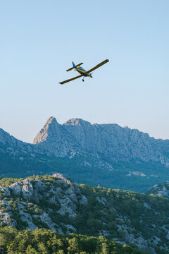 A small yellow firefighting plane flies over the mountains 