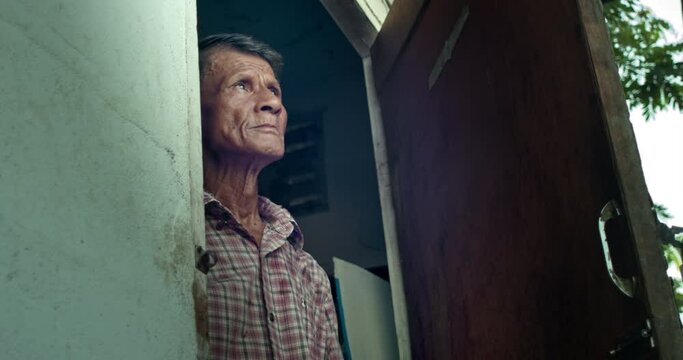 An Asian man who is an elderly worker, opened the door and looked up at the sky as if something had happened to the earth's atmosphere. Used in film concepts, humanity, documentaries and others.