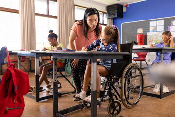 Asian teacher assists a Caucasian girl in a wheelchair at school, after class - obrazy, fototapety, plakaty