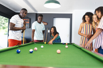 Diverse group of friends enjoy a game of pool, with a young African American man taking his shot