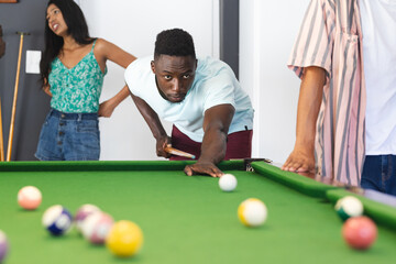 Young African American man focuses on a pool shot, with a young biracial woman watching
