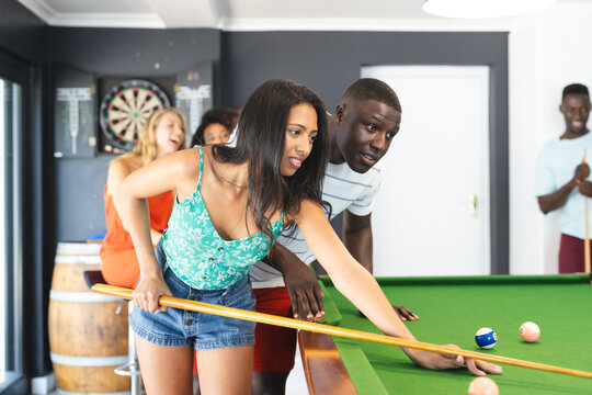 Biracial woman in a green top plays pool, guided by a young African American man - Powered by Adobe