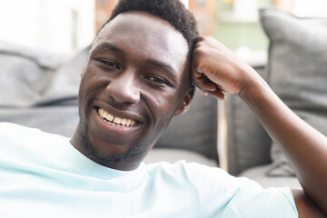 Young African American man smiles broadly, showcasing a casual style in a light blue shirt