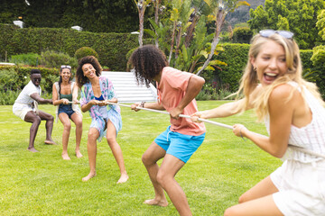 Fototapeta premium Diverse group of friends enjoy a tug-of-war game on a sunny day