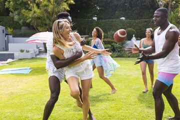 Young Caucasian woman catches a football, cheered on by a young African American man