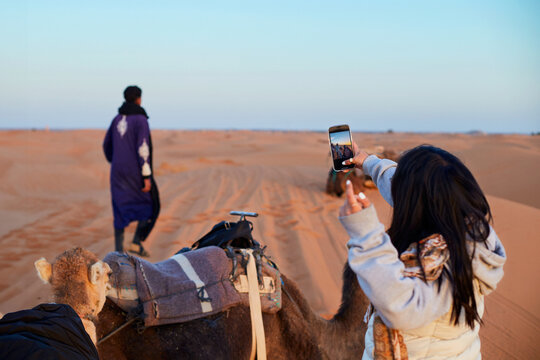 A girl is taking photos during a guided camel tour in the desert.