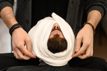 The barber covers the client face with a hot wet towel to steam off the beard.