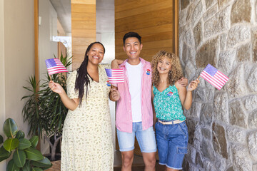 Diverse friends hold American flags at a home entrance