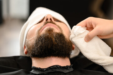 Hairdresser stylist wipes the remains of shaving gel with towel after shaving the beard