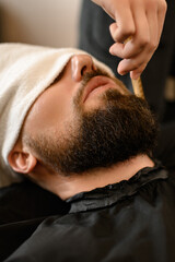 Barber combs beard with comb while shaving Caucasian man