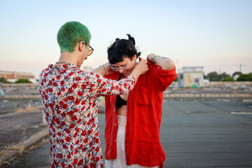 Queer friends helping each other get dressed at public abandoned place