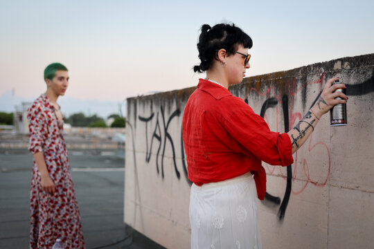 Young couple spraying ink: painting wall with graffitti