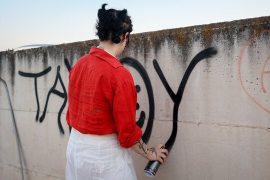 Anonymous cool young woman spraying ink: graffiti on the wall