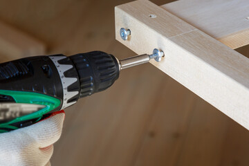 Assembling wooden furniture with a screwdriver. Screwing screws into a wooden part. Close-up.