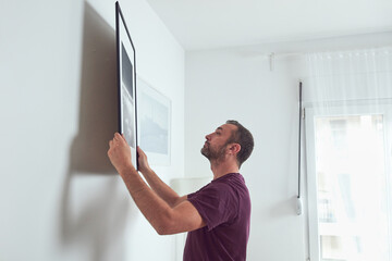 Man hanging pictures on the wall, cleaning and remodeling apartment.