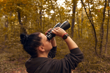 Woman using binoculars for birdwatching and observing other animals in nature.