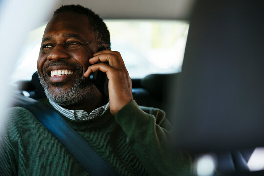 Cheerful middle age man talking on smartphone in car