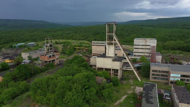 Aerial drone view of old abandoned overgrown coal mine. The shaft tower and desolate concrete buildings of mining factory. Decarbonization, green deal in the modern world during the energy crisis.