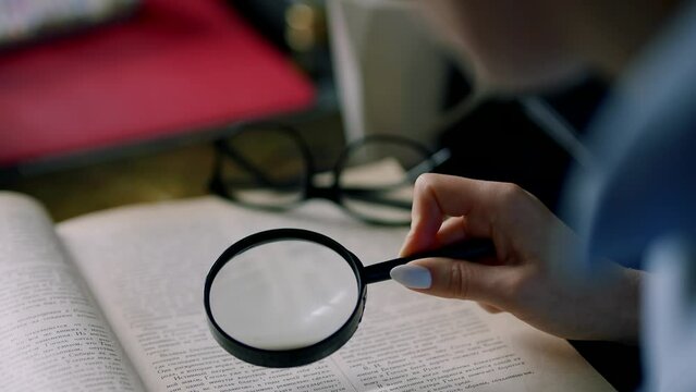 Woman reads book with magnifying glass in library	