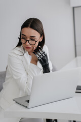 Focused professional with bionic arm using laptop, merging technology and human touch in a...