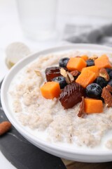 Delicious barley porridge with blueberries, pumpkin, dates and almonds in bowl on table, closeup