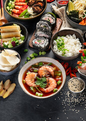 Traditional Asian food table. Spring roll, rice, shrimp, sushi, vegetables, meat on dark background