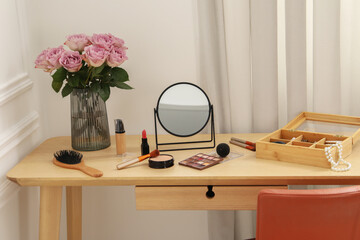 Mirror, cosmetic products, box of jewelry and vase with pink roses on wooden dressing table in makeup room