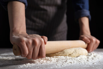 Obraz na płótnie Canvas Making bread. Woman rolling dough at table on dark background, closeup