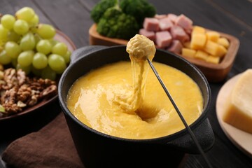 Dipping piece of ham into fondue pot with melted cheese on table, closeup