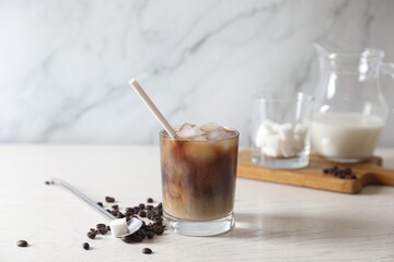 Refreshing iced coffee with milk in glass, beans, spoon and sugar cube on white wooden table