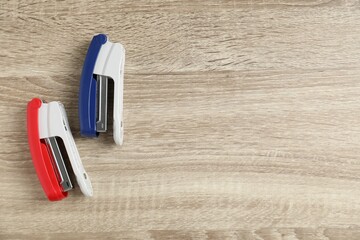 Color staplers on wooden table, flat lay. Space for text