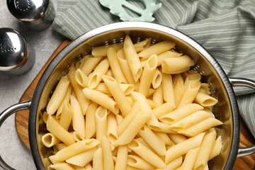 Delicious penne pasta in colander and spices on table, flat lay