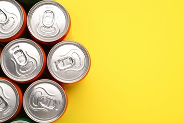 Energy drink in cans on yellow background, top view. Space for text