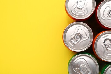Energy drink in cans on yellow background, top view. Space for text