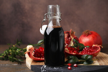 Tasty pomegranate sauce in bottle, fruits and branches on wooden table, closeup