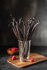 Vanilla beans in the glass on a wooden board and raspberries